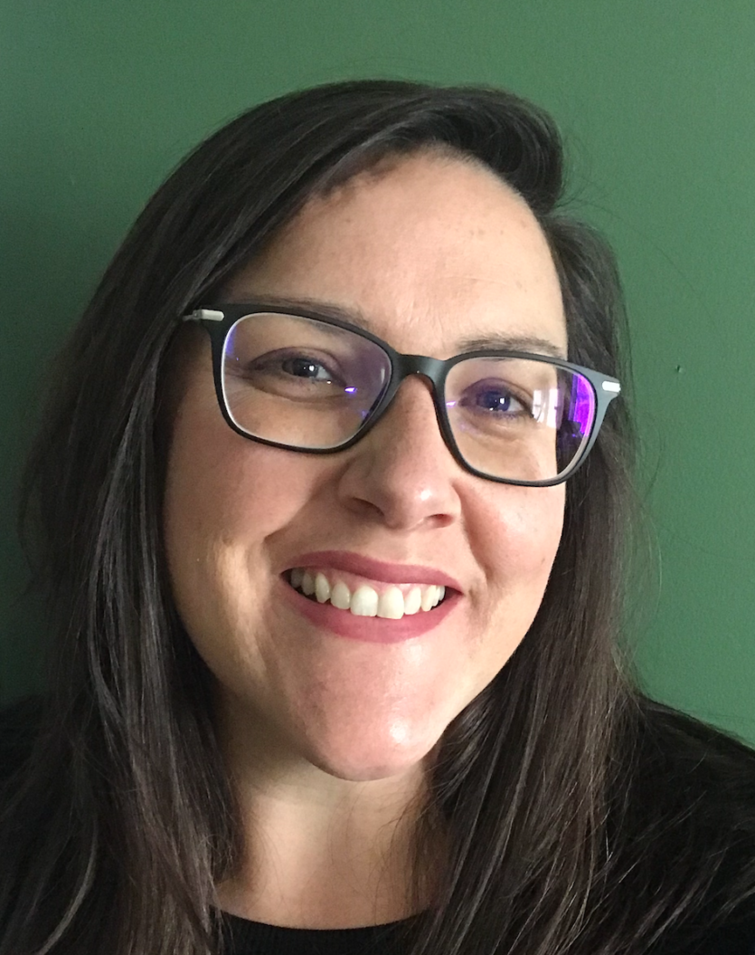 Celia Overby smiling with long brown hair and black glasses.